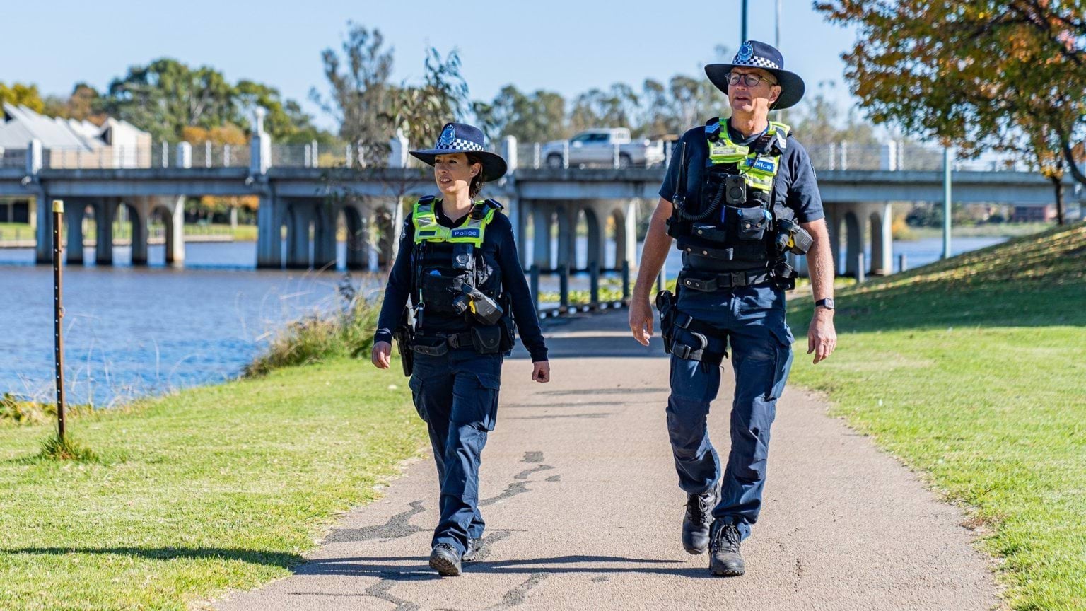 Two officers in police uniform walking on a footpath next to a river.