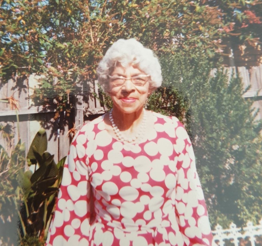 May Rosser smiling while wearing a pink and white outfit in a garden