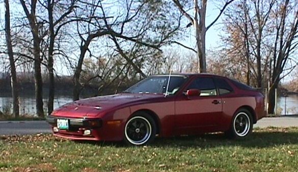 A photo of a vehicle similar to Nick’s red Porsche coupe. It is a dark red colour, has silver rimmed wheels and is parked on a patch of grass.  