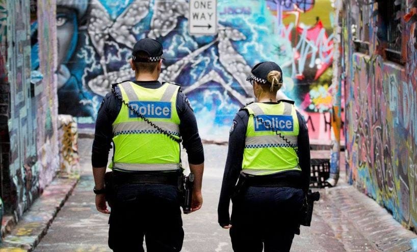 Two police officers in uniform walking through a laneway.