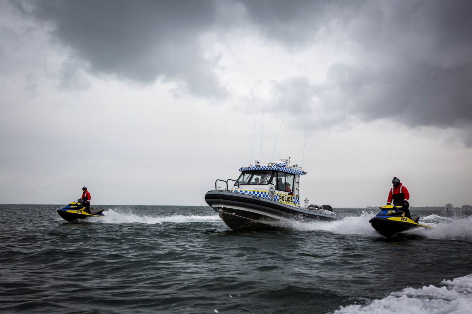 Water police boat and two water police speedboats driving on the open ocean. 