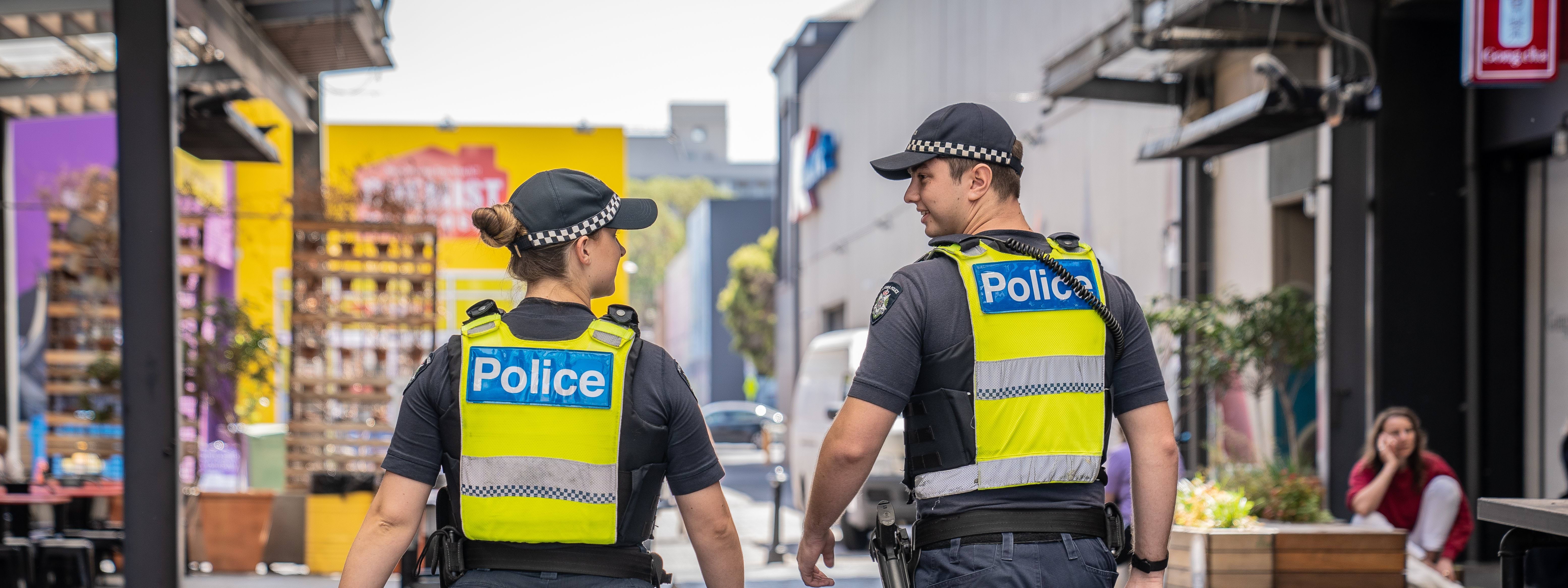 Two police officers in uniform walking through a laneway.