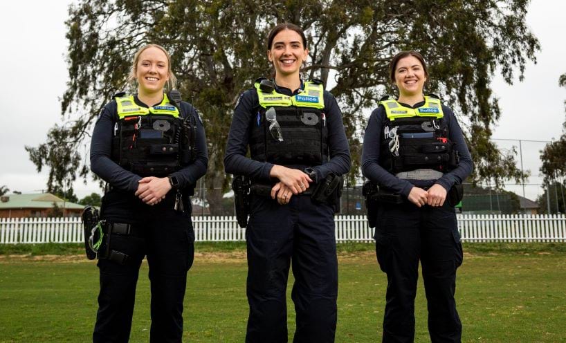 Three female officers in police uniform stand facing the camera and smiling. 