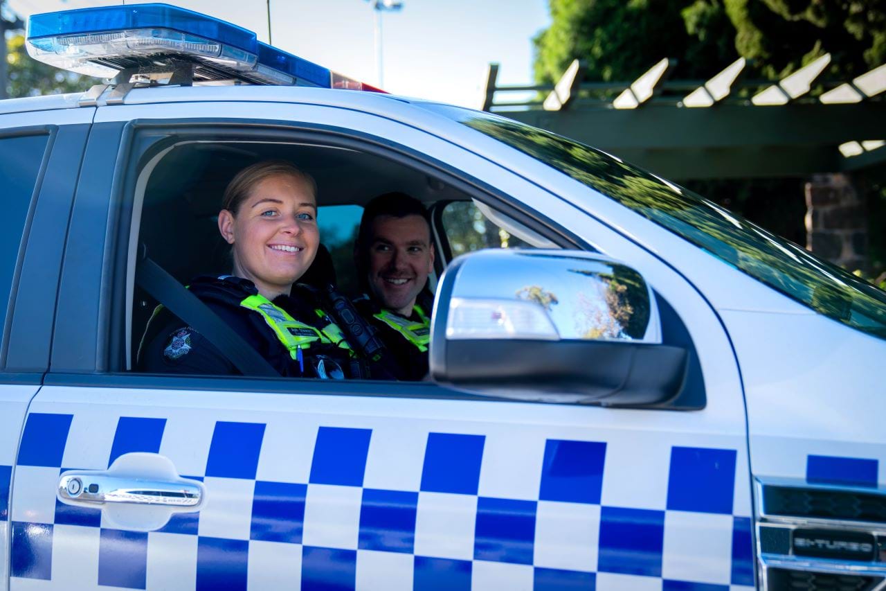 Two officers sit smiling through the open window of a police vehicle. 