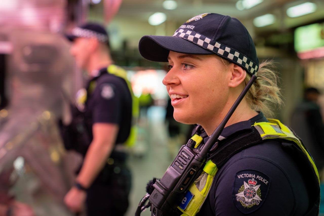 A uniformed police officer is smiling towards a butcher shop counter, presumably smiling at someone working there. There is another officer out of focus in the background. 