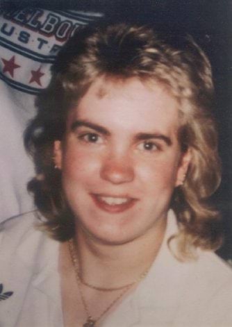 Sarah MacDiarmid, with neck length blonde/brown hair, wearing a gold chain and a white collared shirt.