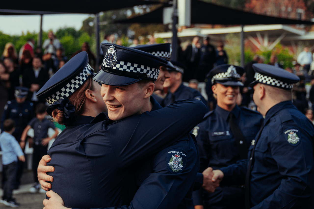 Two recruits in dress uniform hug each other at a Victoria Police graduation ceremony at the Academy. 