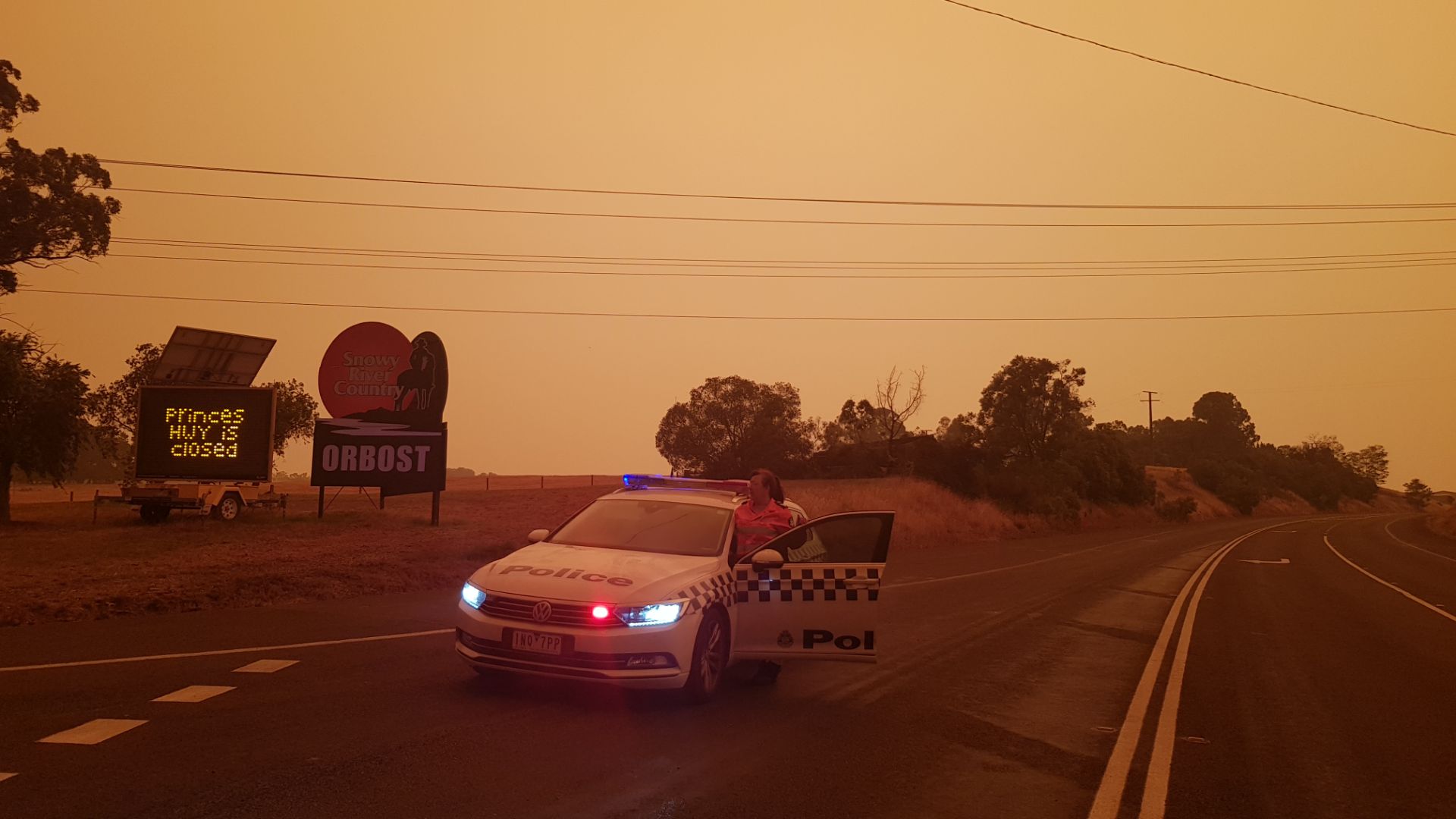 Victorian bushfires 2019-2020 - Orange sky above police car on deserted road