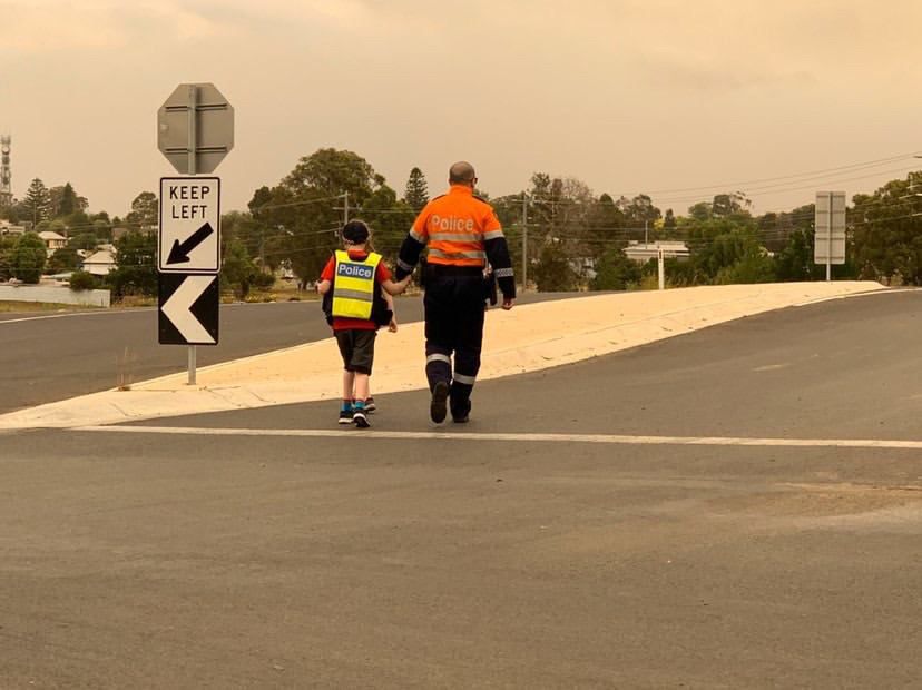 Victorian bushfires 2019-2020 - Police officer taking a boy in police vest across deserted road