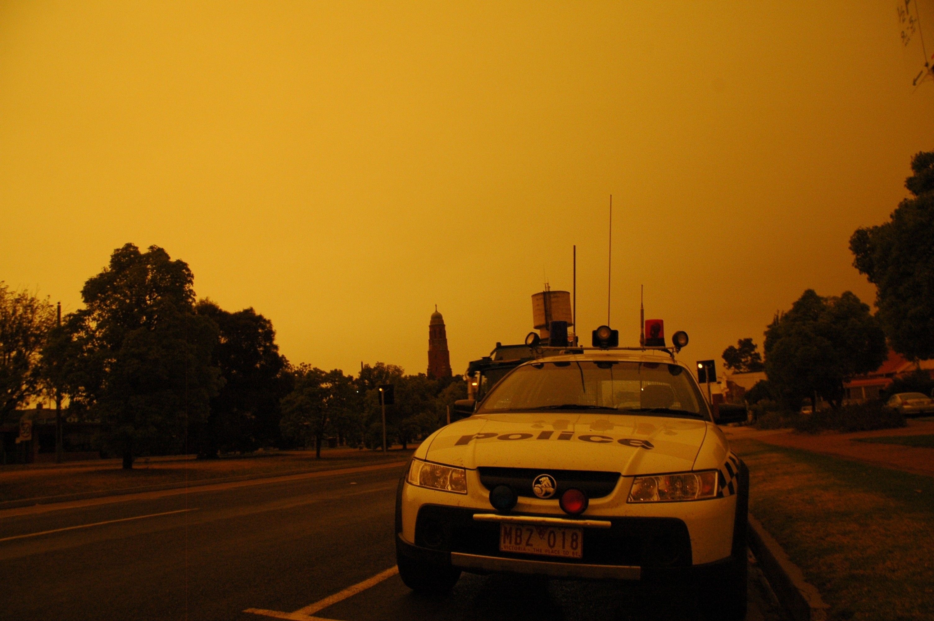 Victorian bushfires 2019-2020 - Orange bushfire sky above a police car parked on empty street