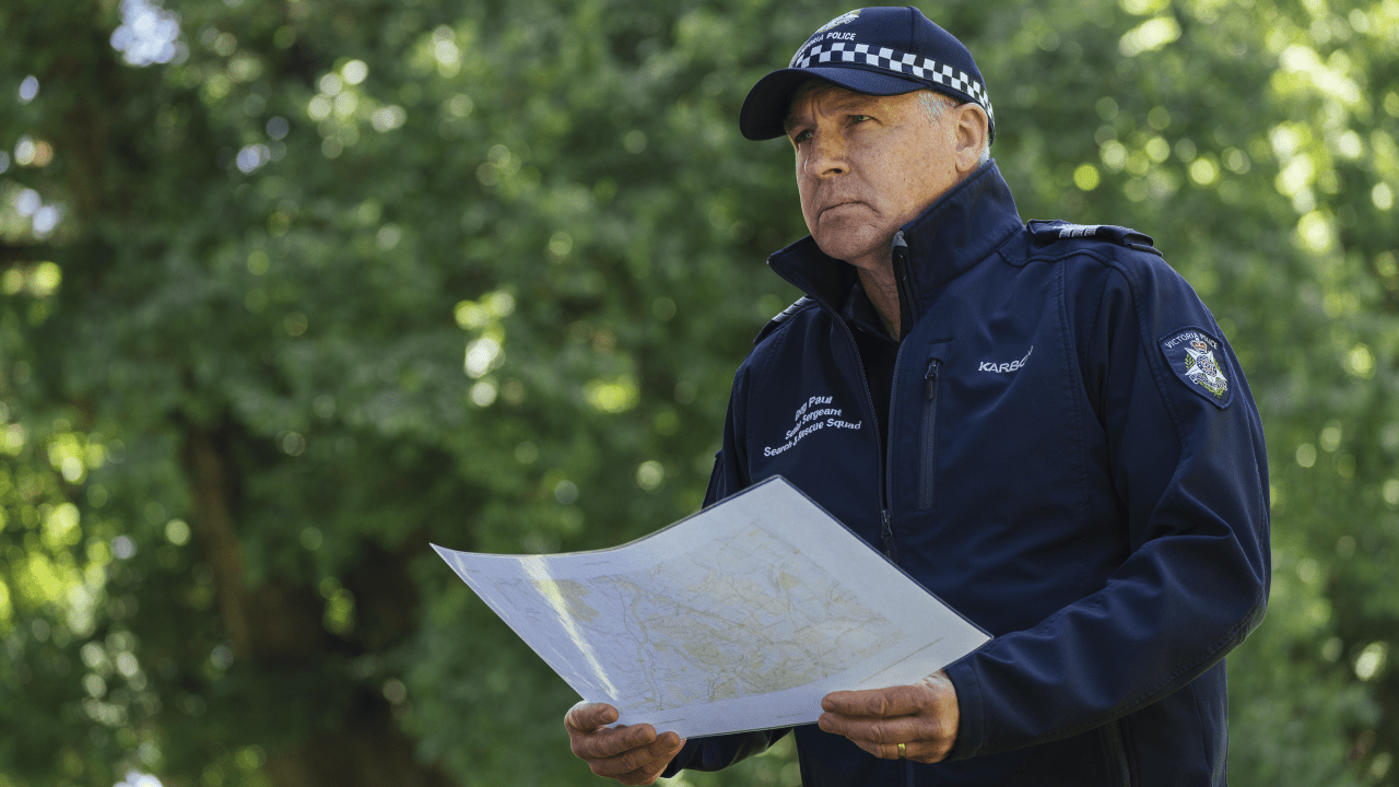 Senior Sergeant Greg Paul, wearing police uniform, holding a map. 