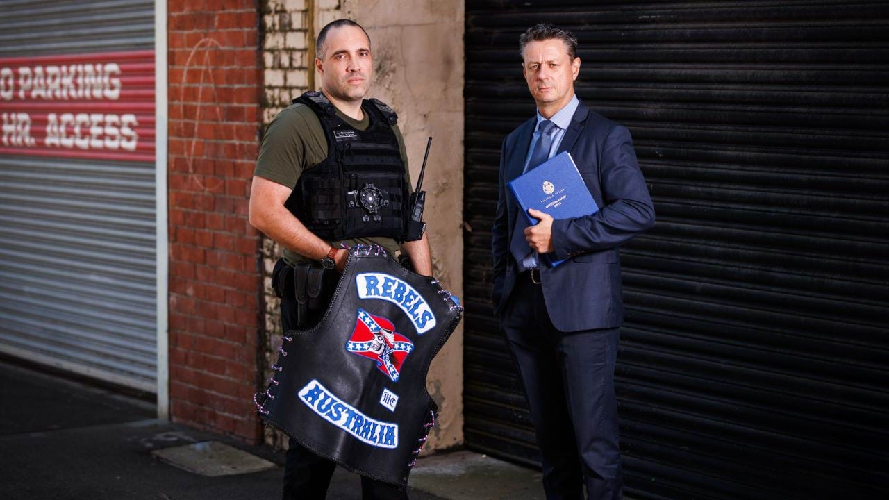 Members of Victoria Police standing, holding a Rebels Australia bikie jacket.