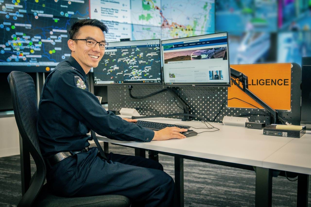 Officer sitting at a desk, with two screens, looking at a map with various locations, and Intelligence sign post. 