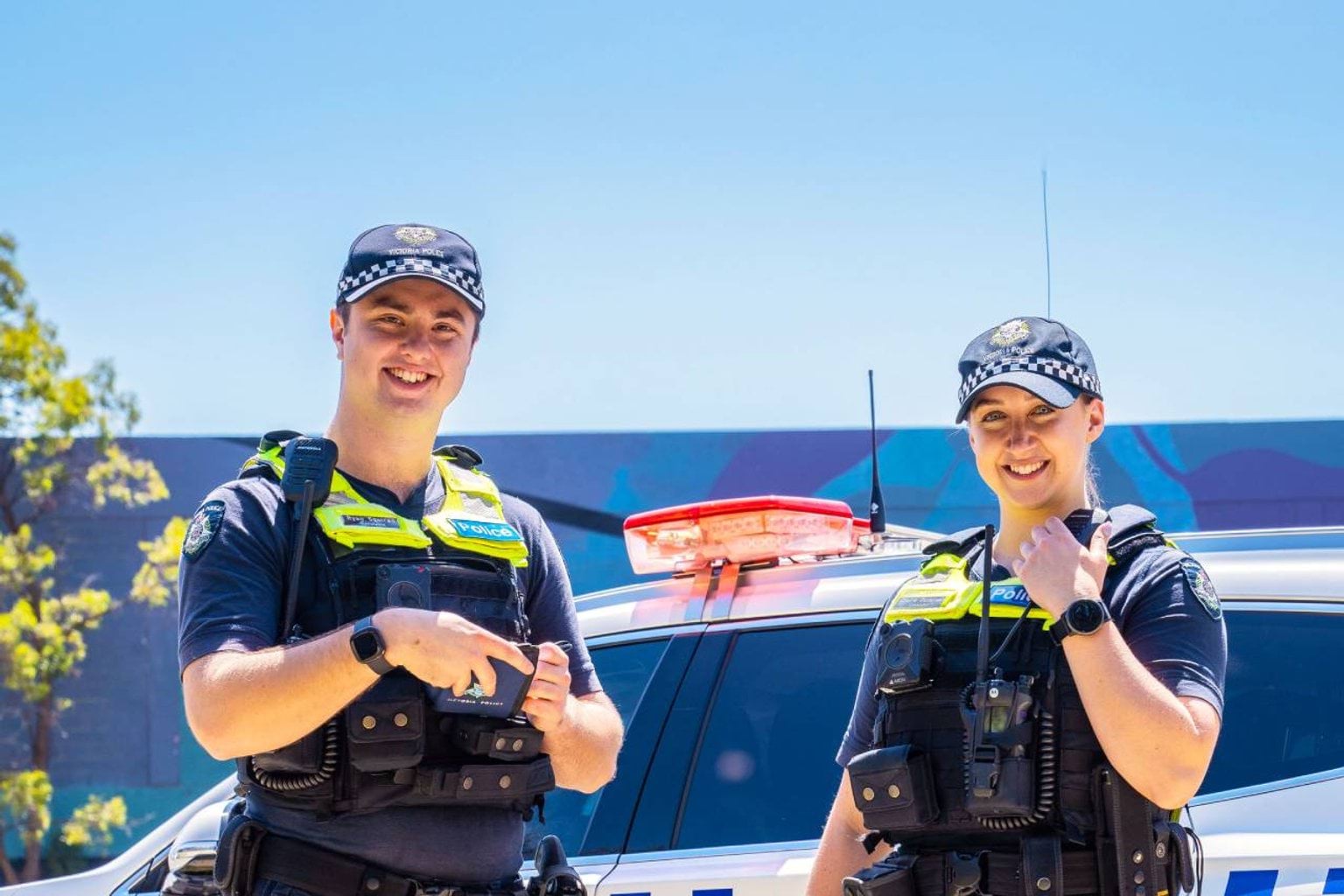 Two smiling officers outside next to a police car