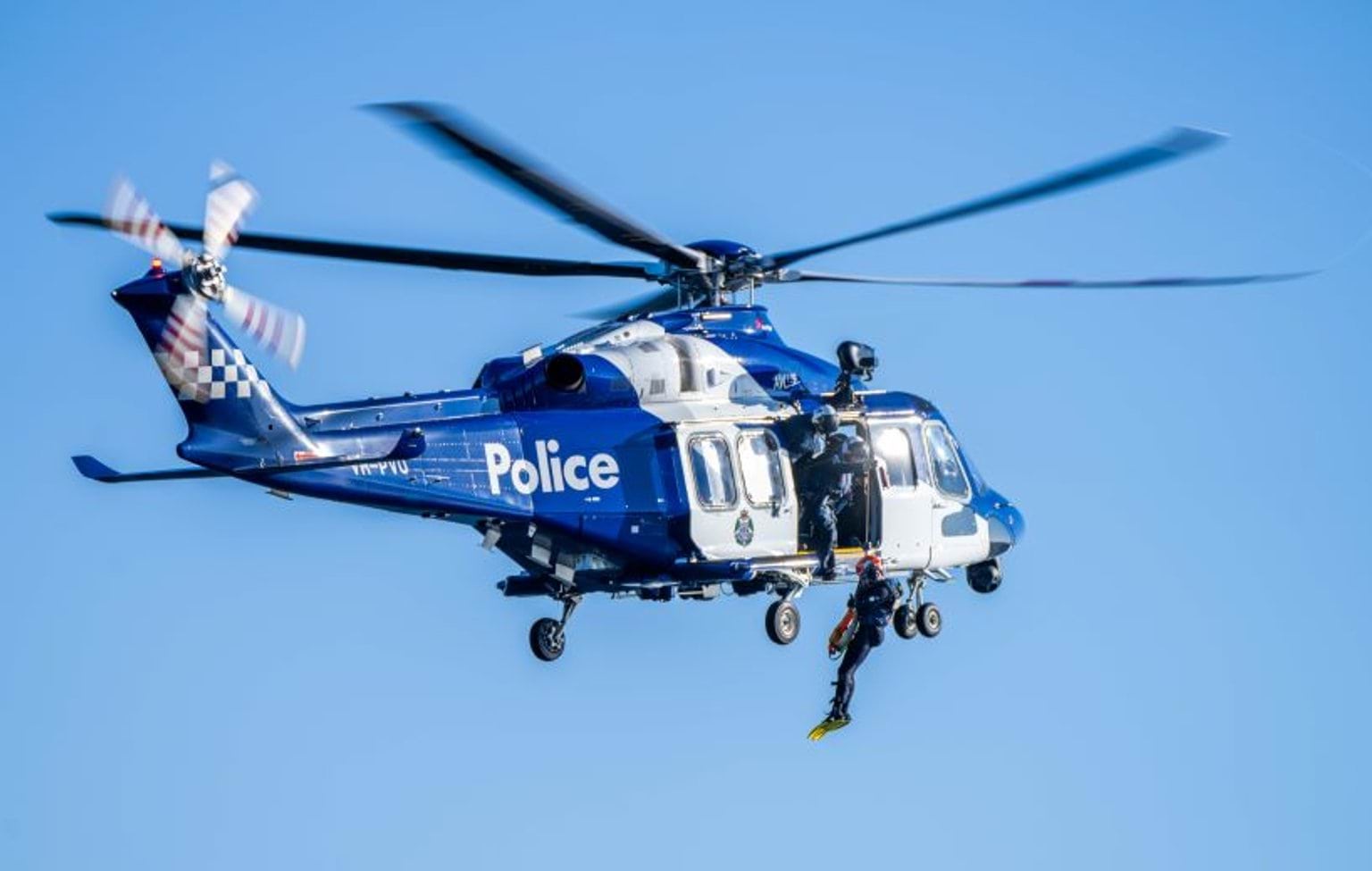 A Victoria Police member being winched out of a police helicopter over the water