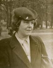 Katherine Mackay wearing a work cap and suit, holding a handbag. 